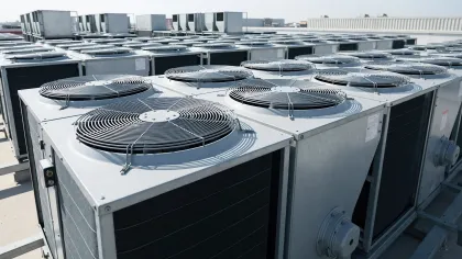 Rows of large industrial HVAC units with fans on top installed on a rooftop under clear sky