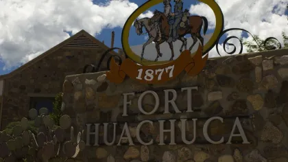 Stone sign for Fort Huachuca with two horseback riders illustration and the year 1877 under a partly cloudy sky.