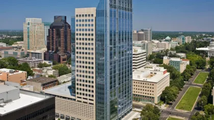 Modern glass skyscraper and surrounding downtown office buildings under clear blue sky in an urban cityscape