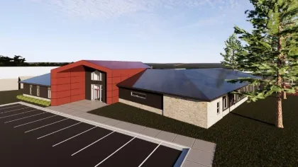 Modern building with a red entrance, large parking lot, and surrounding greenery under a blue sky.