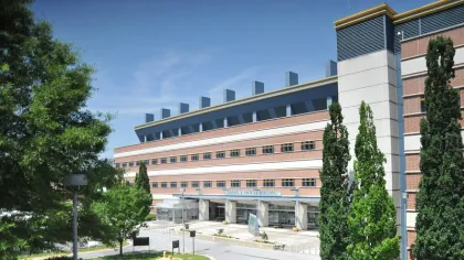 Modern multi-story medical building with clear sky and surrounding green trees during daytime.