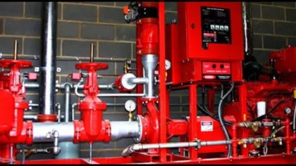 Industrial red fire sprinkler control system with valves, pipes, gauges, and electrical panel in utility room.