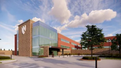 Modern brick and glass institutional building with large windows under a partly cloudy blue sky.