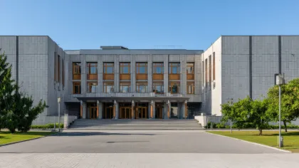 Modern government building with symmetrical design, large windows, and surrounding green trees under clear blue sky.
