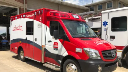 Red and white UCHealth paramedic ambulance parked outside a fire station under a blue sky.