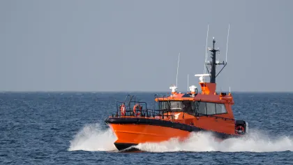 Orange pilot boat speeding through ocean water with waves and a clear sky in the background