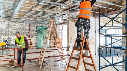 Construction workers installing ceiling framework in a building under renovation with ladders and scaffolding.