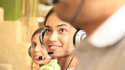 Smiling customer service representatives wearing headsets in a busy call center environment.