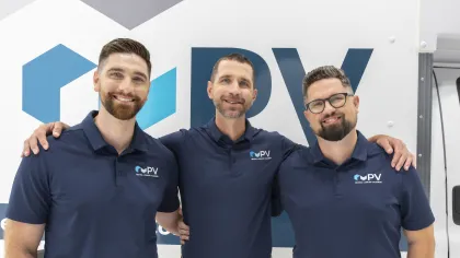 Three men in navy blue PV polo shirts posing and smiling in front of a PV branded background