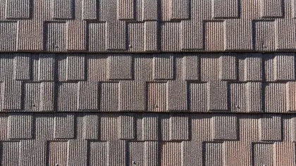 Close-up of brown textured roof shingles arranged in overlapping horizontal rows under sunlight.