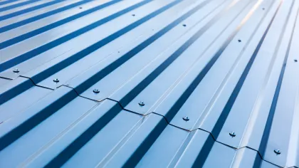 Close-up of blue corrugated metal roofing panels with screws securing overlapping ridges in sunlight.