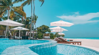 a pool with lounge chairs and umbrellas by a beach