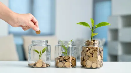 a hand holding a plant in a jar with coins
