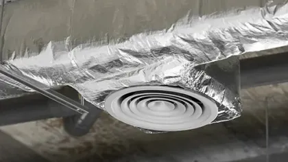 Round ceiling air vent surrounded by insulated silver ductwork in an industrial building interior.