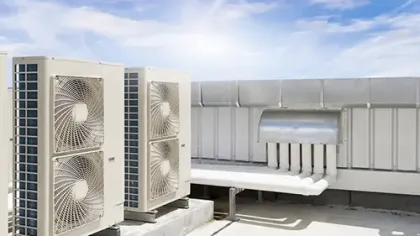 Two large outdoor air conditioning units installed on a rooftop with metal ductwork and blue sky background.