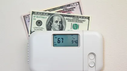 Thermostat set at 67 degrees with US twenty and one hundred dollar bills behind it representing energy savings.
