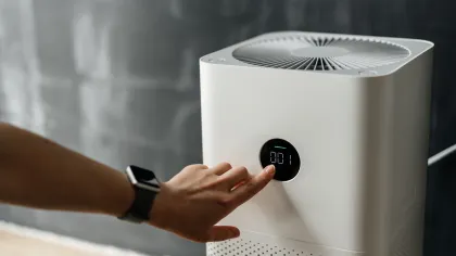 Person adjusting settings on a modern white air purifier with digital display in a home environment.