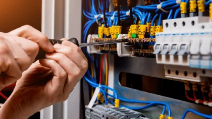 Electrician using screwdriver to install or repair wiring in an electrical control panel with blue cables and yellow labels