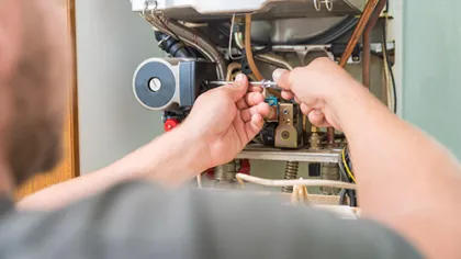 Technician repairing a gas boiler with tools focusing on internal components and wiring