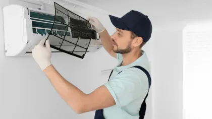 Technician wearing gloves removing air filter from wall-mounted air conditioner for cleaning or maintenance.