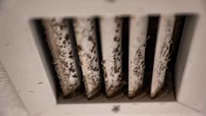 Close-up of a dirty, dust-covered air vent grille with visible grime on the slats.