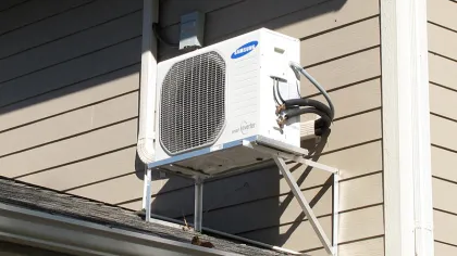 Samsung smart inverter air conditioning unit mounted on beige siding exterior with metal support bracket.