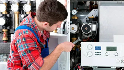 Technician in plaid shirt repairing a residential boiler system using a wrench in a utility room.
