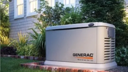 Generac Guardian Series home backup generator installed outdoors beside a house with garden and lawn.