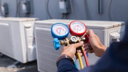 Technician using pressure gauges to check HVAC system performance on outdoor air conditioning units.