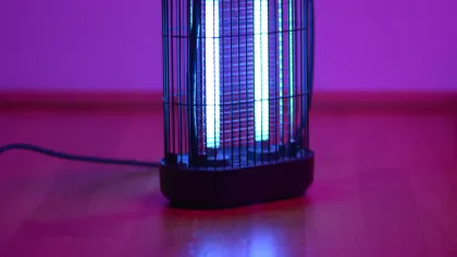 Electric bug zapper glowing blue on wooden floor with purple background lighting