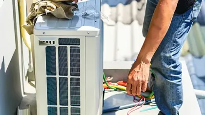 Technician installing or repairing an outdoor air conditioning unit with tools and cables on a rooftop.