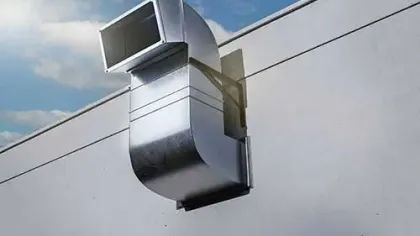 Shiny metal air duct or ventilation pipe protruding from a white building wall against a blue sky
