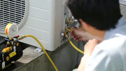 Technician connecting yellow hoses to HVAC unit gauges for air conditioning maintenance outdoors