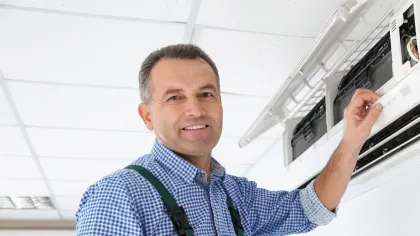 Technician in green overalls repairing or installing a wall-mounted air conditioning unit indoors with a screwdriver.