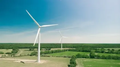 Two large white wind turbines in a green rural landscape under a clear blue sky on a sunny day