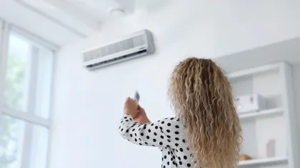 Woman with curly hair pointing remote at wall-mounted air conditioner in bright modern room