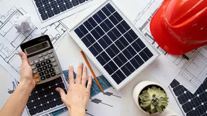 Hands using calculator over solar panel blueprints with solar panels, red safety helmet, and succulent plants