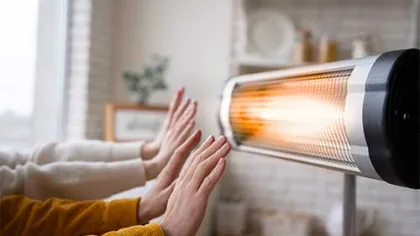 People warming hands in front of an electric heater in a cozy indoor setting with blurred background.