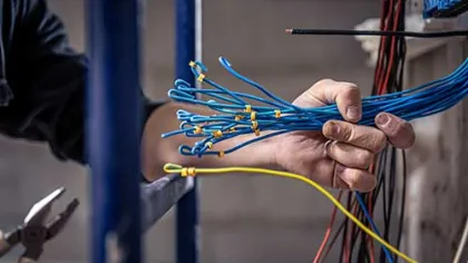 Technician holding and organizing blue electrical wires with a yellow wire in an indoor industrial setting.