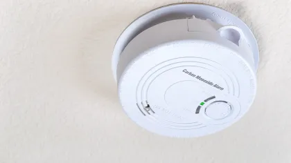 White carbon monoxide alarm mounted on a textured ceiling with status indicator light.
