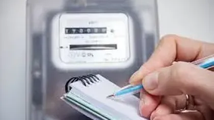 Hand holding a pen writing on a notepad with an electricity meter in the background.
