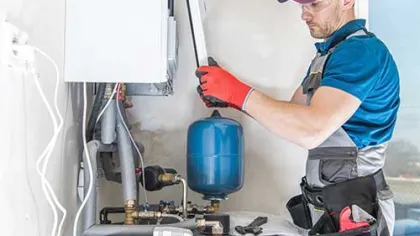 Technician repairing a home boiler system with tools, wearing safety glasses and gloves indoors.