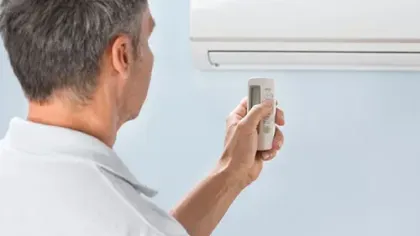 Man using remote control to adjust wall-mounted air conditioner in a light blue room