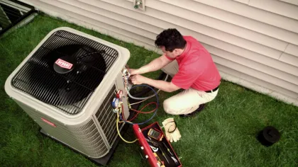 Technician repairing a Bryant air conditioning unit outside a house on green grass near siding wall.