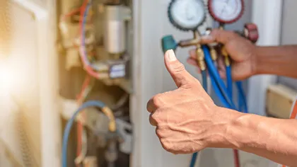 Technician repairing HVAC system with pressure gauges, showing thumbs up in sign of job well done.