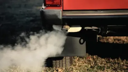 Vehicle exhaust pipe emitting white smoke over dry grass, highlighting pollution and emissions.