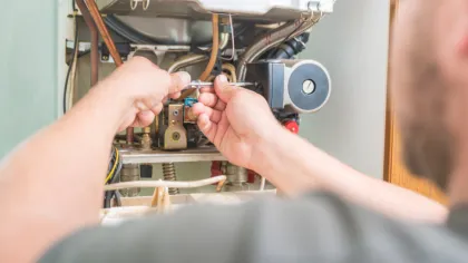 Technician using wrench to repair internal components of a heating system boiler unit indoors.