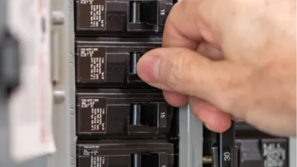 Hand turning off a circuit breaker switch in an electrical panel for safety or maintenance.
