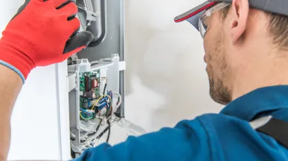 Technician wearing red gloves repairs and inspects electrical appliance circuit board closely indoors.