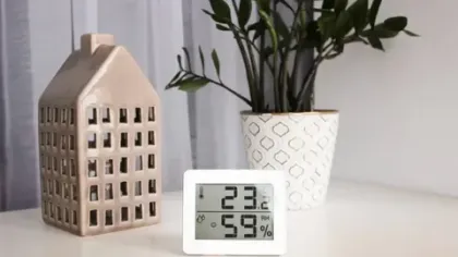 Digital hygrometer and thermometer showing 23.2°C and 59% humidity on a white table with plant and decorative house.